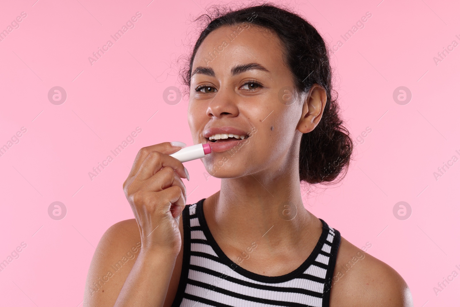 Smiling woman applying lip balm onto her lips on pink background Photo of Smiling woman applying lip balm onto her lips on pink background