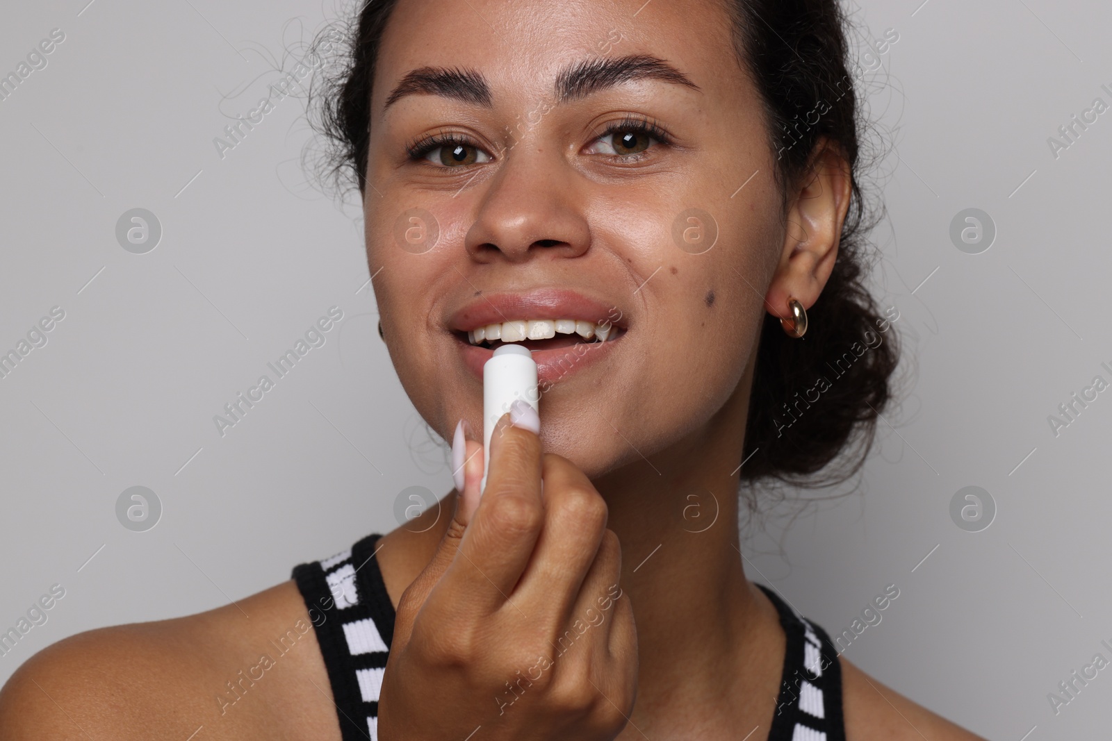 Smiling woman applying lip balm onto her lips on grey background, closeup Photo of Smiling woman applying lip balm onto her lips on grey background, closeup