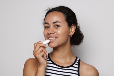 Photo of Smiling woman applying lip balm onto her lips on grey background