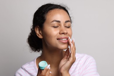 Photo of Smiling woman applying lip balm onto her lips on grey background