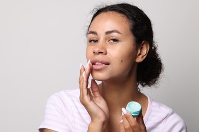 Photo of Beautiful woman applying lip balm onto her lips on grey background