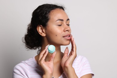 Photo of Beautiful woman applying lip balm onto her lips on grey background
