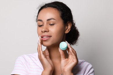 Photo of Smiling woman applying lip balm onto her lips on grey background