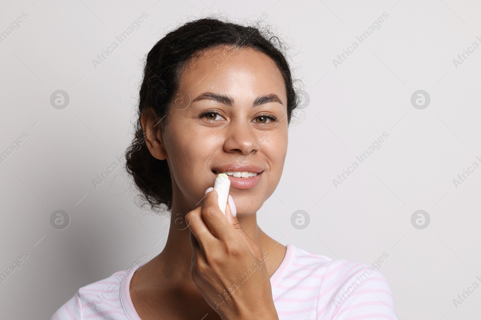 Smiling woman applying lip balm onto her lips on grey background Photo of Smiling woman applying lip balm onto her lips on grey background