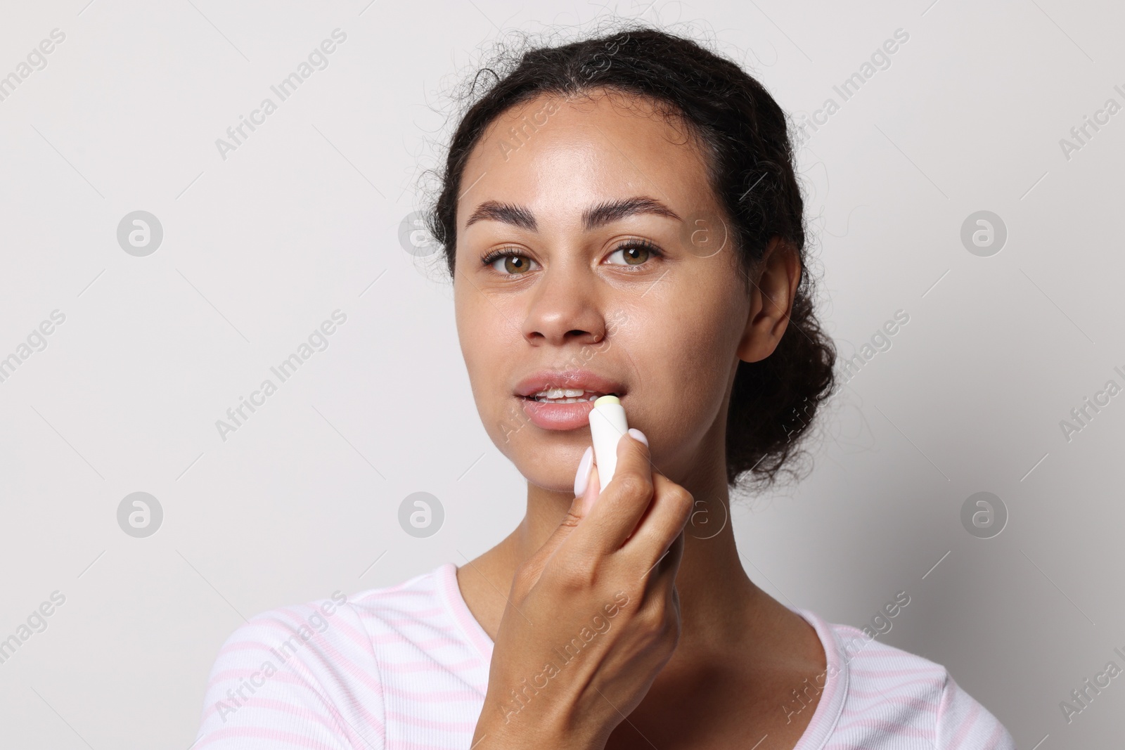 Beautiful woman applying lip balm onto her lips on grey background Photo of Beautiful woman applying lip balm onto her lips on grey background