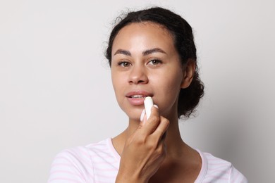 Photo of Beautiful woman applying lip balm onto her lips on grey background
