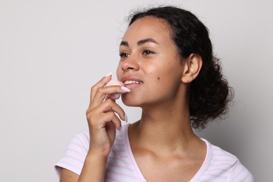 Photo of Smiling woman applying lip balm onto her lips on grey background
