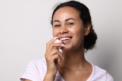 Photo of Smiling woman applying lip balm onto her lips on grey background