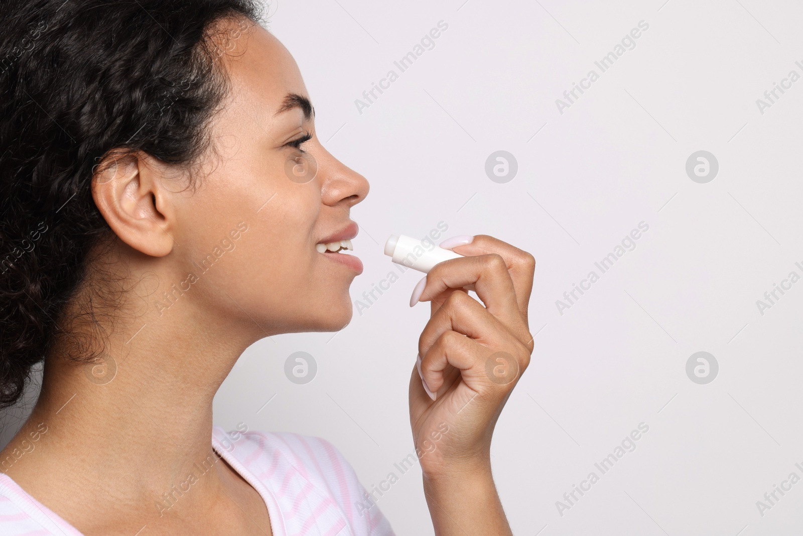 Smiling woman applying lip balm onto her lips on grey background, closeup. Space for text Photo of Smiling woman applying lip balm onto her lips on grey background, closeup. Space for text