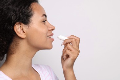 Photo of Smiling woman applying lip balm onto her lips on grey background, closeup. Space for text