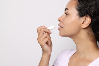 Photo of Beautiful woman applying lip balm onto her lips on grey background, closeup. Space for text