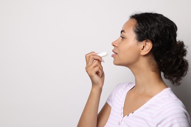 Photo of Beautiful woman applying lip balm onto her lips on grey background. Space for text
