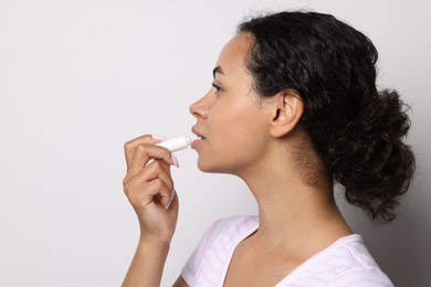 Photo of Beautiful woman applying lip balm onto her lips on grey background
