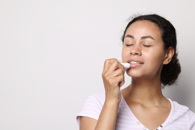 Photo of Smiling woman applying lip balm onto her lips on grey background. Space for text