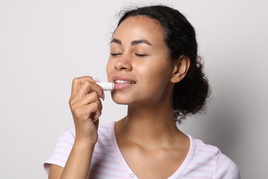 Photo of Smiling woman applying lip balm onto her lips on grey background
