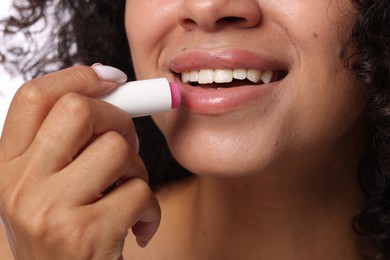 Photo of Smiling woman applying lip balm onto her lips, closeup