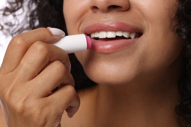 Photo of Smiling woman applying lip balm onto her lips, closeup