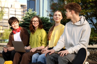 Photo of Teenagers with different devices on bench in park