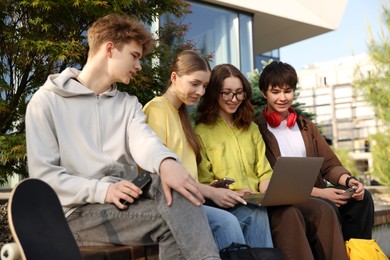 Photo of Teenagers with different devices on bench in park