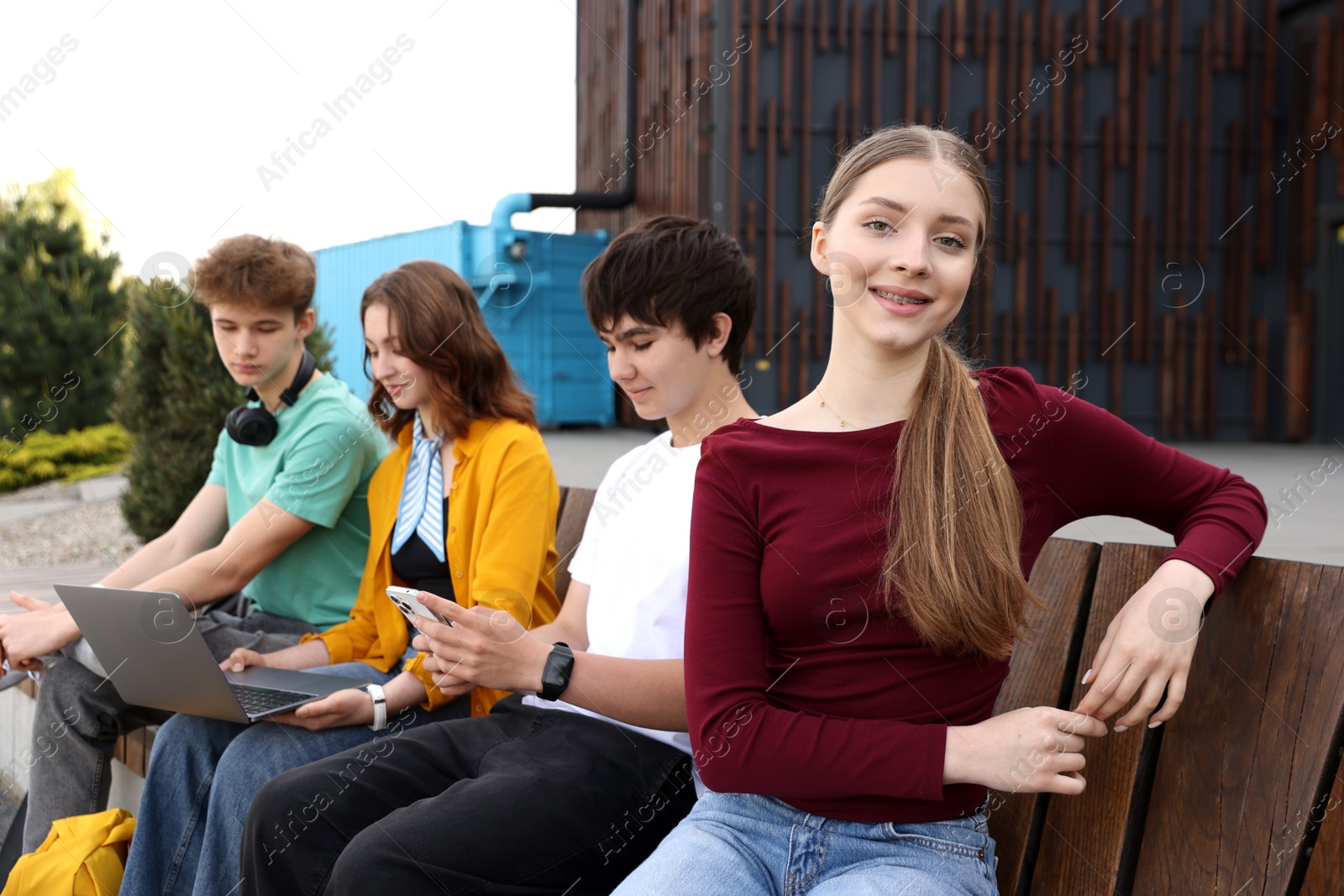 Teenagers with different devices on bench outdoors Photo of Teenagers with different devices on bench outdoors