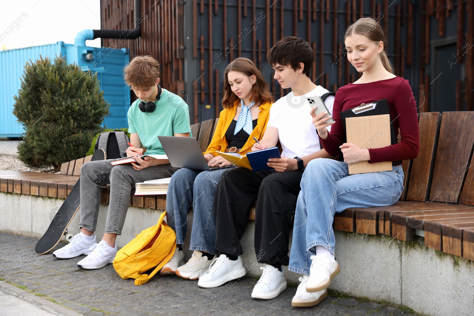Group of teenagers studying together on bench outdoors Photo of Group of teenagers studying together on bench outdoors
