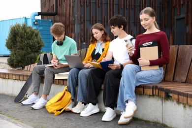Photo of Group of teenagers studying together on bench outdoors
