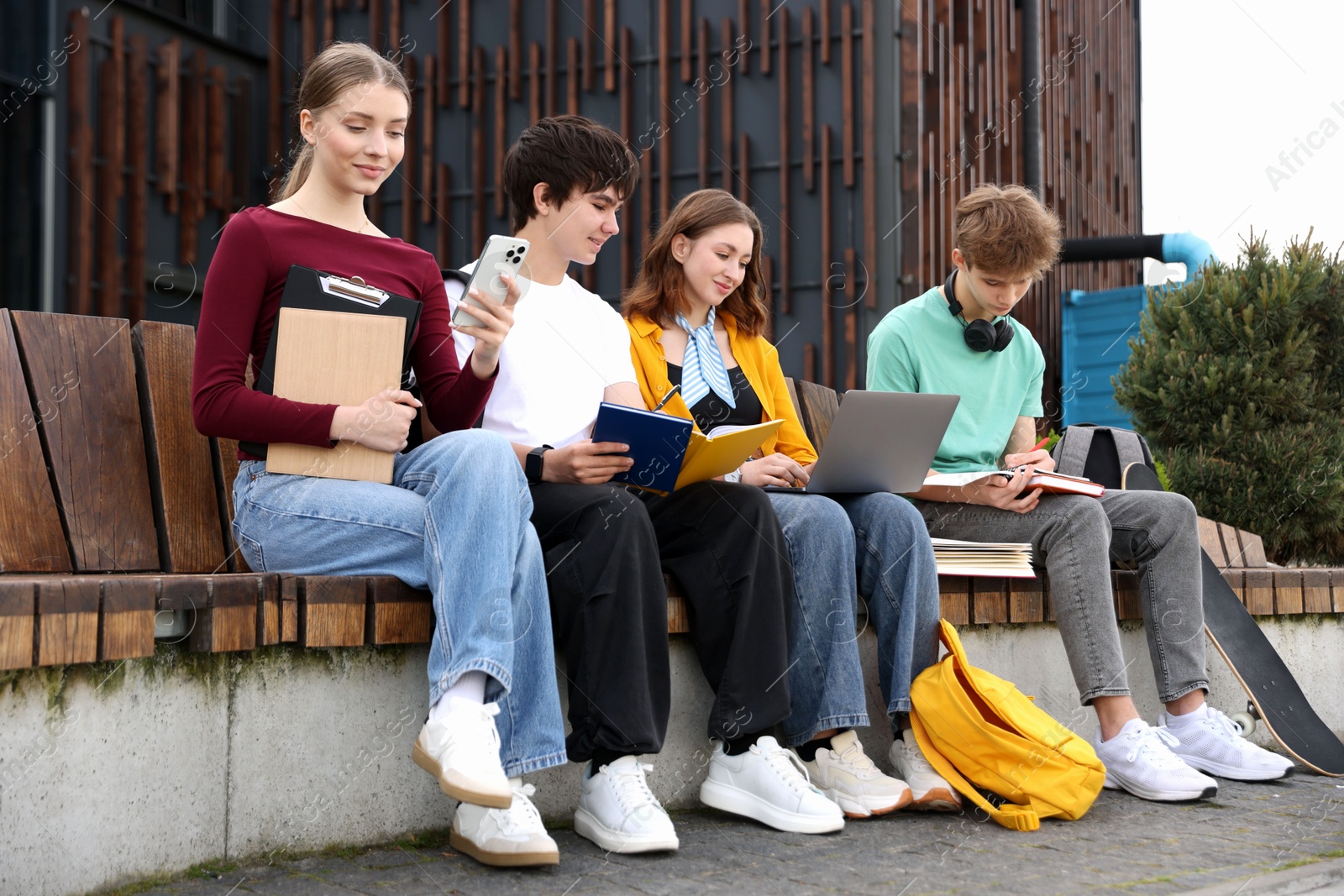 Group of teenagers studying together on bench outdoors Photo of Group of teenagers studying together on bench outdoors