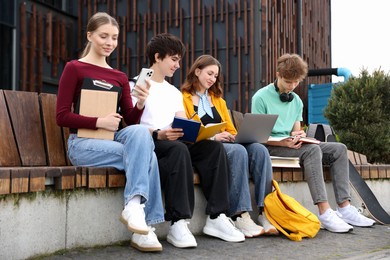 Photo of Group of teenagers studying together on bench outdoors