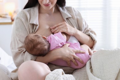 Photo of Mother breastfeeding her newborn baby on bed indoors, closeup