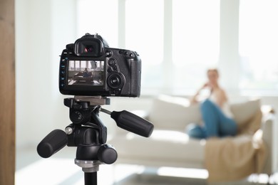 Photo of Woman on sofa in studio, focus on video camera recording her
