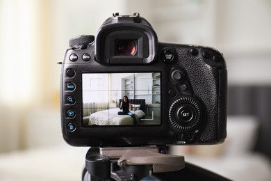 Photo of Woman sitting on bed in studio, focus on video camera recording her