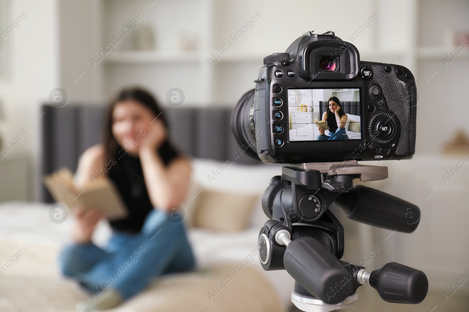Woman reading book on bed in studio, focus on video camera recording her Photo of Woman reading book on bed in studio, focus on video camera recording her