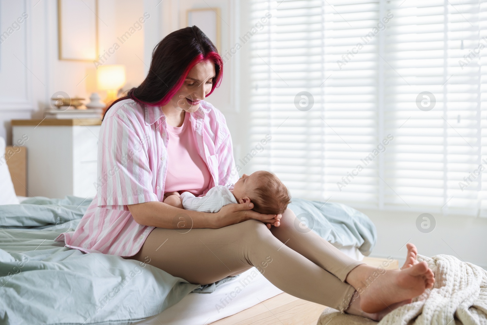 Photo of Mother putting her cute newborn baby to sleep on bed at home