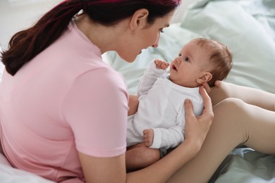 Photo of Mother putting her cute newborn baby to sleep on bed at home, closeup