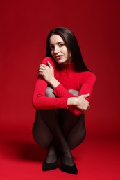 Photo of Full-length portrait of beautiful woman in stylish outfit on red background