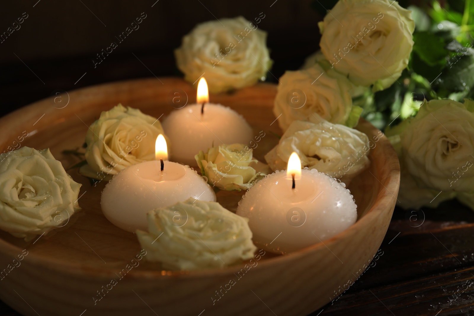 Burning candles, water and rose flowers in bowl on wooden table, closeup Photo of Burning candles, water and rose flowers in bowl on wooden table, closeup