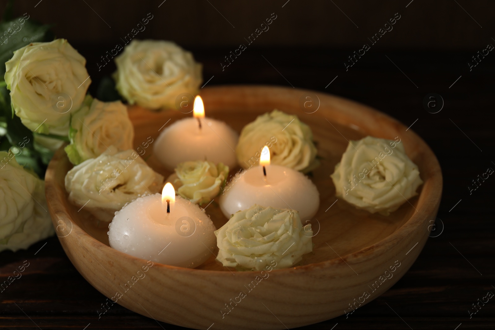 Photo of Burning candles, water and rose flowers in bowl on wooden table, closeup