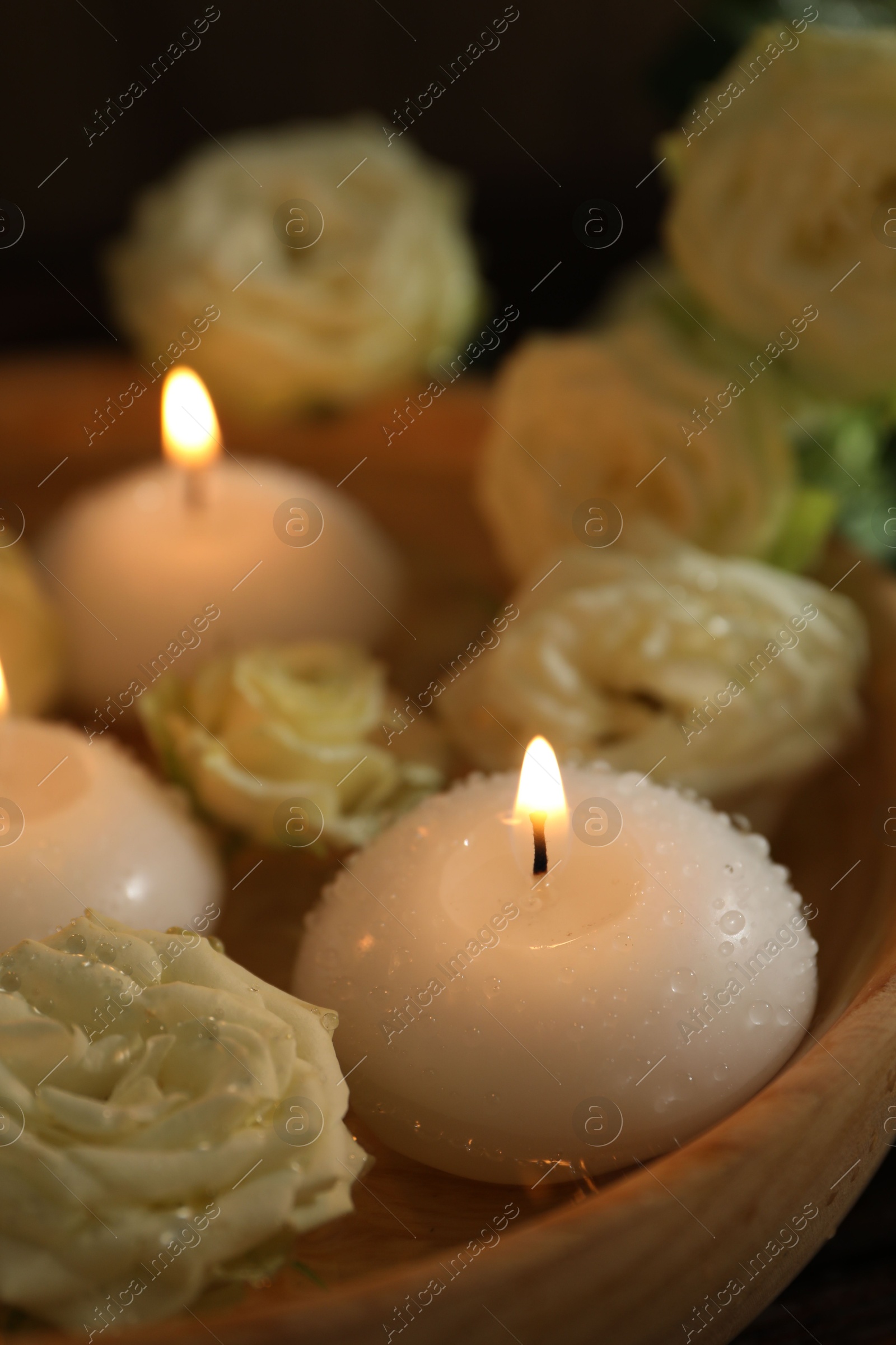 Photo of Burning candles, water and rose flowers in wooden bowl on table, closeup