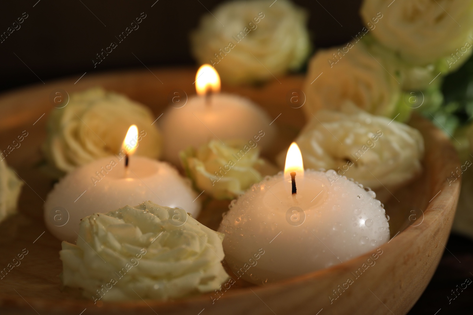 Photo of Burning candles, water and rose flowers in wooden bowl on table, closeup