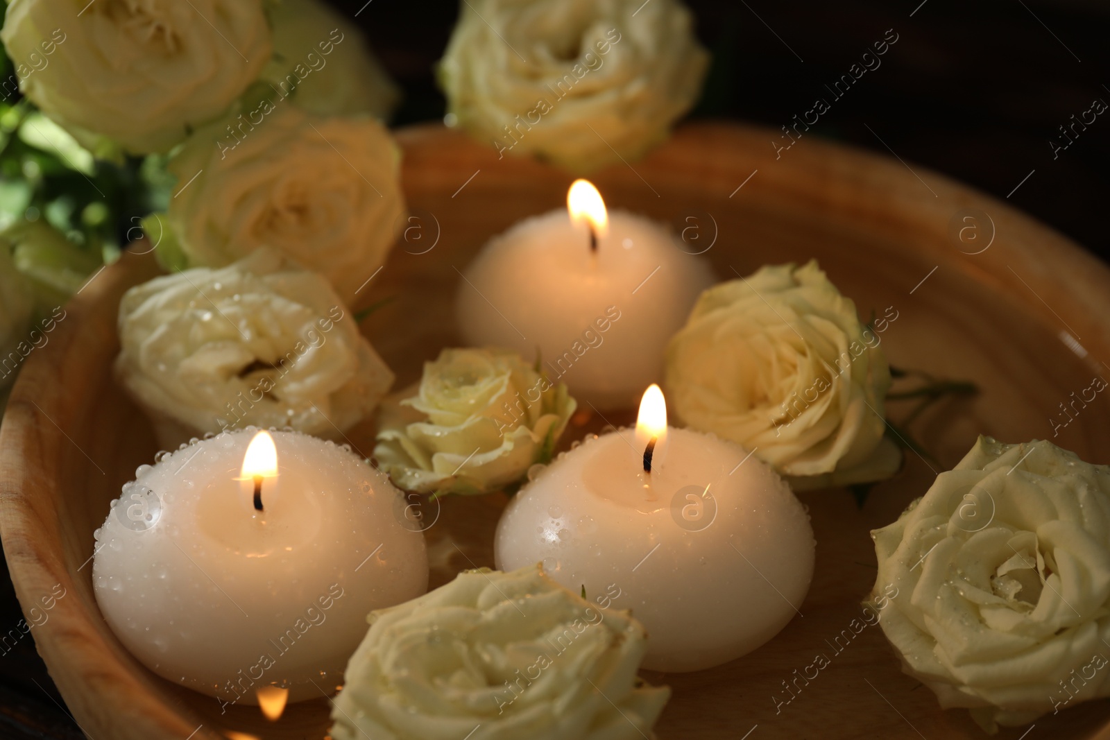 Photo of Burning candles, water and rose flowers in wooden bowl on table, closeup