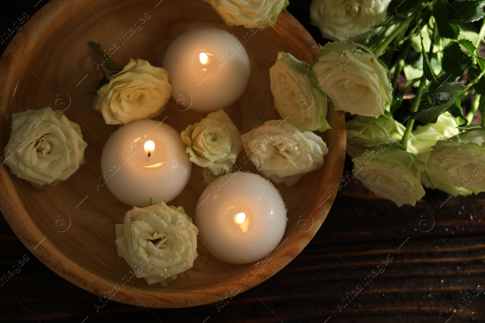 Burning candles, water and rose flowers in bowl on wooden table, flat lay Photo of Burning candles, water and rose flowers in bowl on wooden table, flat lay