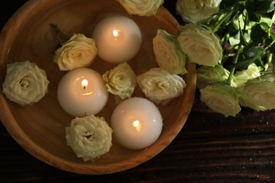 Photo of Burning candles, water and rose flowers in bowl on wooden table, flat lay