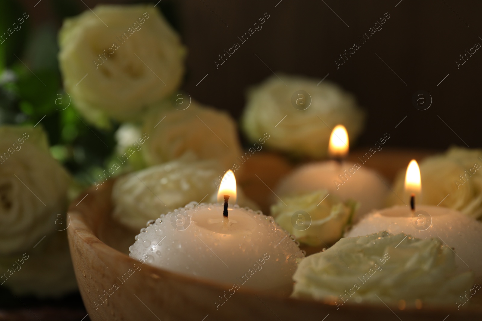 Photo of Burning candles, water and rose flowers in bowl on wooden table, closeup