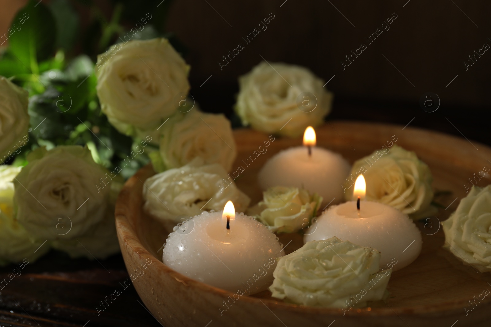 Photo of Burning candles, water and rose flowers in bowl on wooden table, closeup