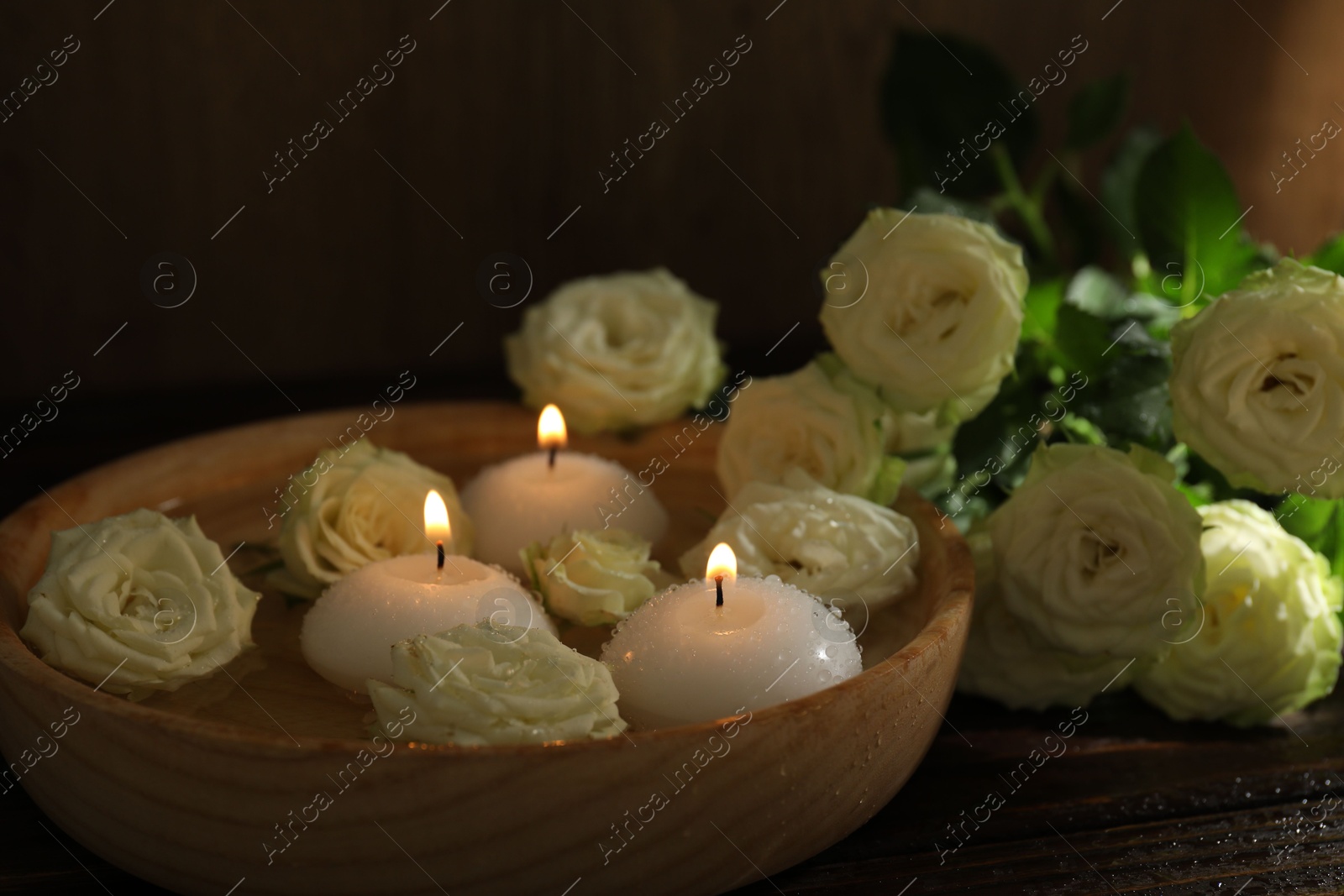Photo of Burning candles, water and rose flowers in bowl on wooden table, closeup
