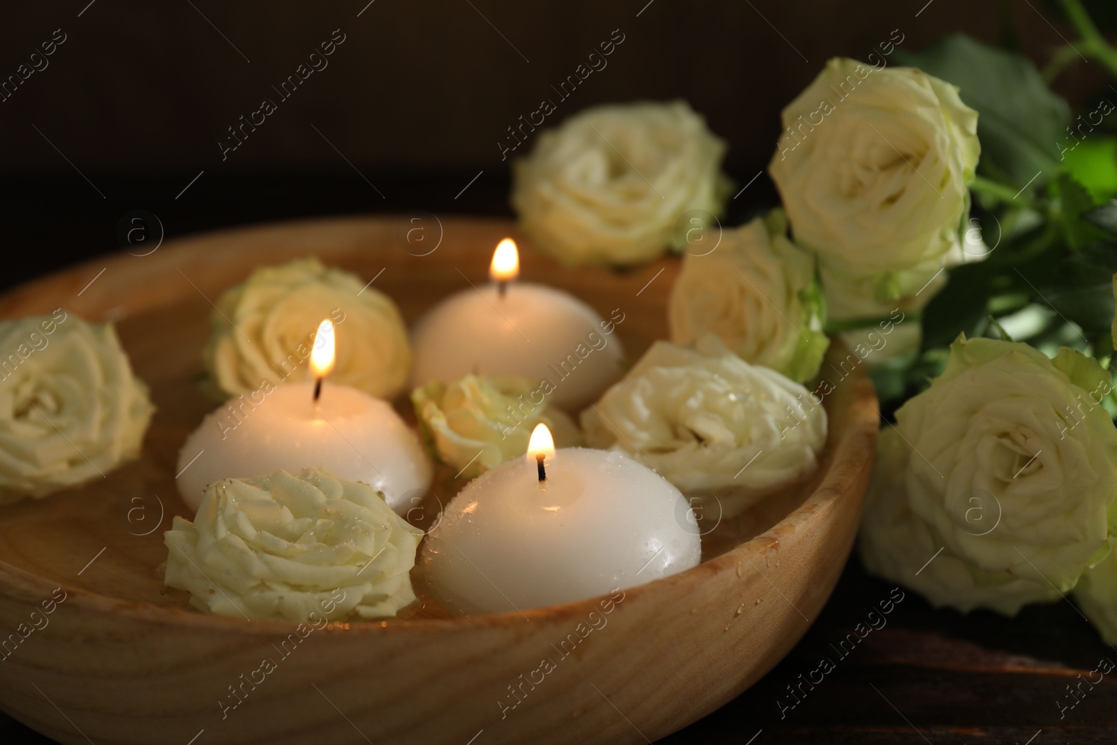 Photo of Burning candles, water and rose flowers in bowl on wooden table, closeup