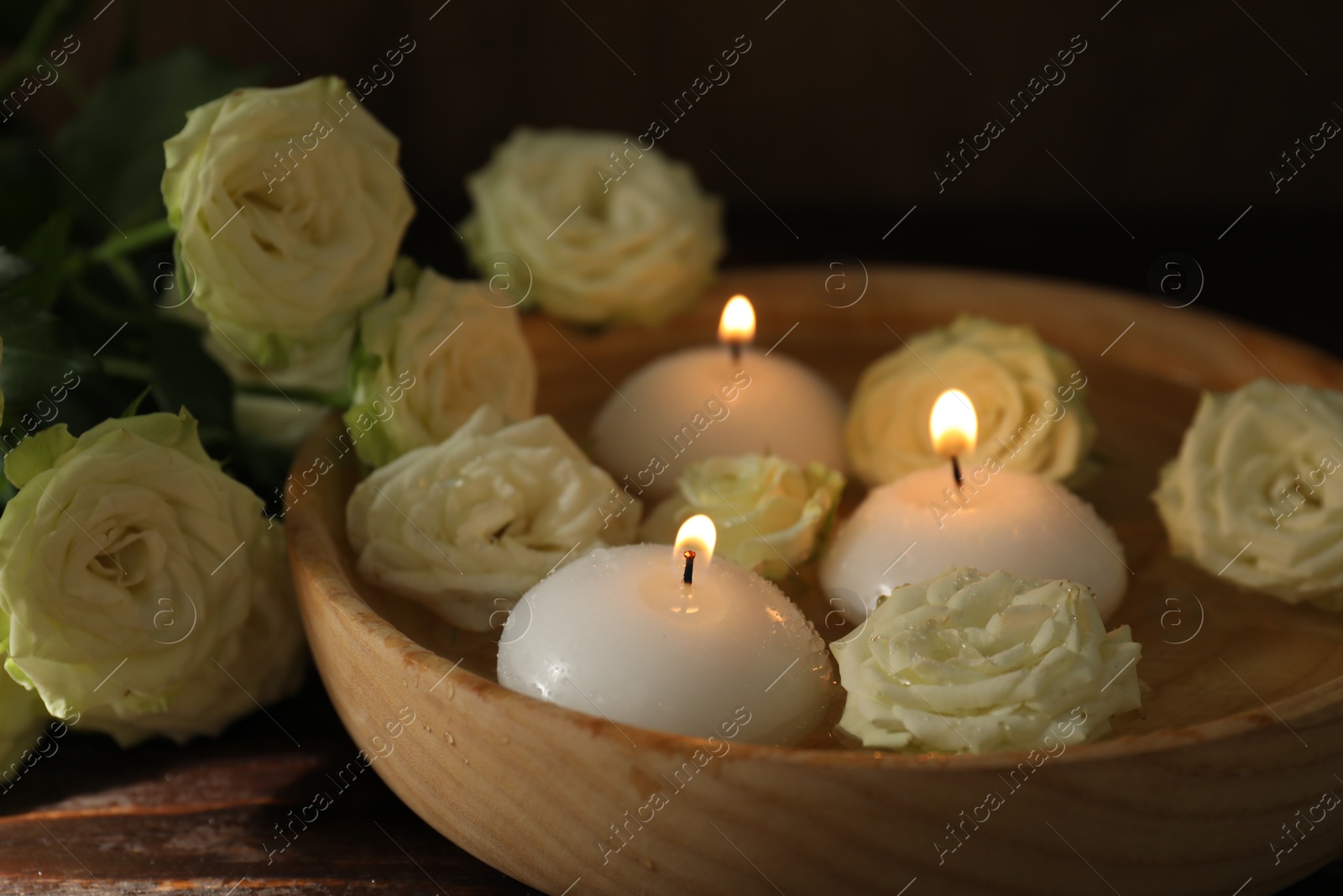 Burning candles, water and rose flowers in bowl on wooden table, closeup Photo of Burning candles, water and rose flowers in bowl on wooden table, closeup