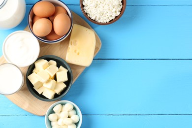 Photo of Different dairy products and eggs on light blue wooden table, flat lay. Space for text
