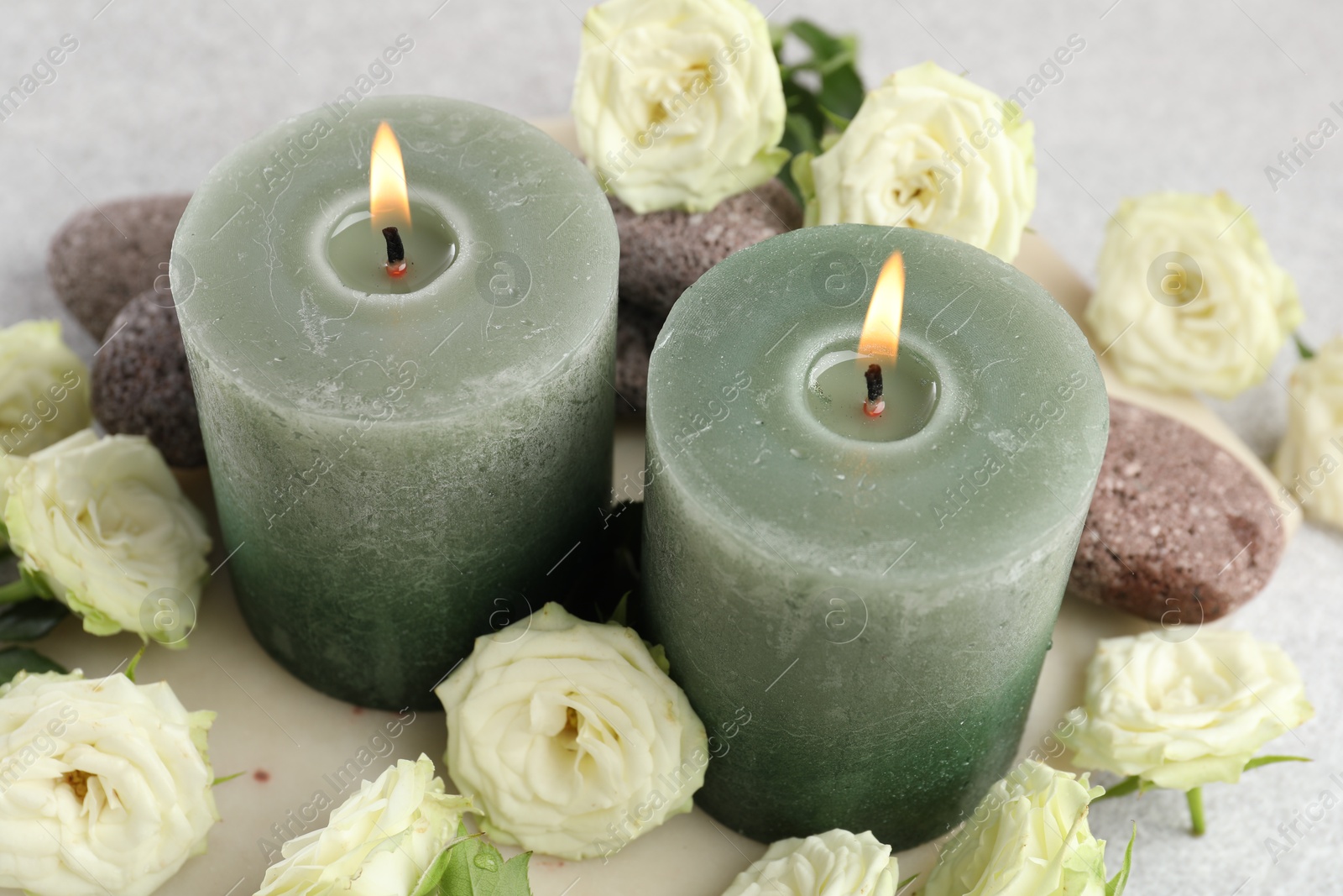 Burning candles, stones and rose flowers on light grey table, closeup Photo of Burning candles, stones and rose flowers on light grey table, closeup