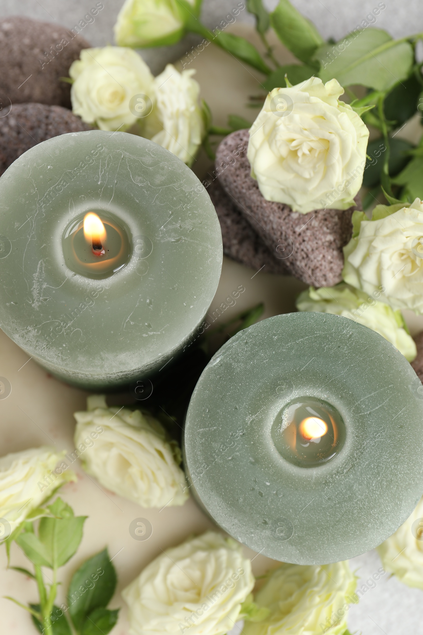 Photo of Burning candles, stones and rose flowers on light grey table, flat lay